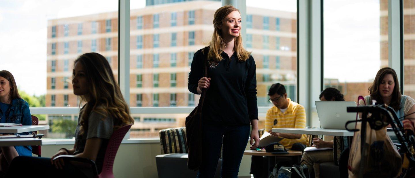 A young woman stands smiling in the Honors College building